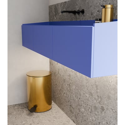 Unidrain Reframe pedalspand i messing placeret på et moderne badeværelsesgulv ved siden af et blåt vægskab.