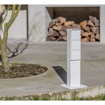 Hvid Niko Hydro stikkontaktsøjle med plads til tre moduler og montageflange, monteret på en terrasse.