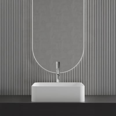 Scandtap Voyage High Classic håndvaskbatteri med blank stålfinish monteret på en hvid, rektangulær håndvask foran en dekorativ, grå ribbet væg.
