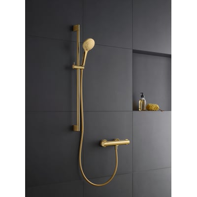 Duravit håndbruser i poleret guld med 3 stråletyper, monteret på en mørkegrå væg ved siden af en sæbedispenser og svamp.