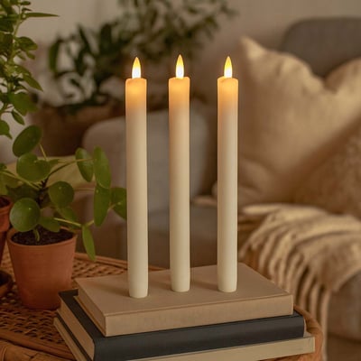 Tre LEDlife LED stearinlys med flammeeffekt står på bøger og skaber hygge i en stueopsætning med planter.