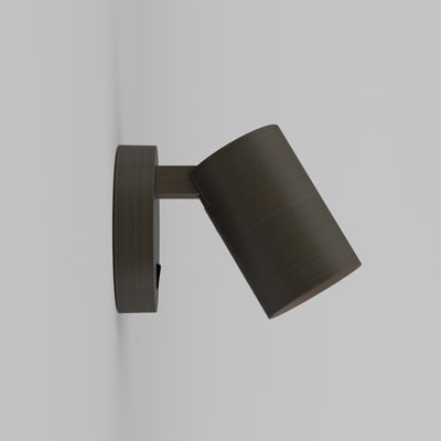 Astro Ascoli single spot lampe i bronze monteret på en lysegrå væg, vist fra siden med lampens justerbare kipfunktion.