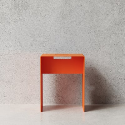 Nichba skammel i orange, pulverlakeret metal med mål 35 x 25 x 45 cm, placeret foran en rå betonvæg.