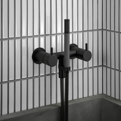 Vola 2-grebsblander i mat sort med keramiske ventiler og brusehoved monteret på en væg med lodrette hvide fliser.