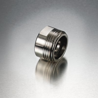 Nordic Quality adapter i messing, bronze, med 1/2" og 3/4" gevind på en reflekterende metallisk baggrund.