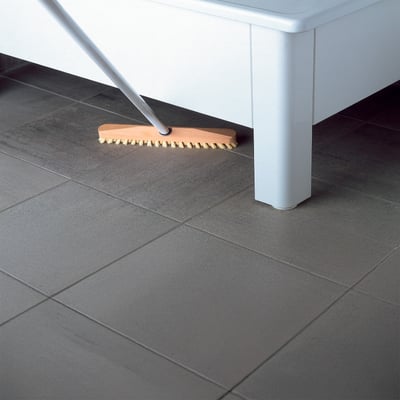 Svedbergs badekar 1204, 1400x700 mm, hvid, bliver rengjort med en kost på et gråt flise gulv.