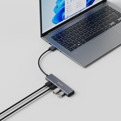 Deltaco USB-A hub i grå aluminium med fire USB 3.0 porte tilsluttet en bærbar computer, med to USB-enheder indsat.