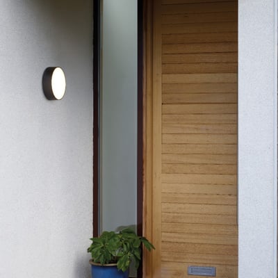 Astro 8022 Kea Round 250 sort LED væg- og loftlampe monteret ved en døråbning med en grøn plante foran.