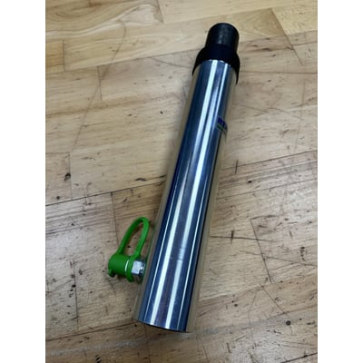 En blank, rustfri stål hydraulisk cylinder med en grøn plastik holder og en sort top hviler på et træbord med synlige årer.