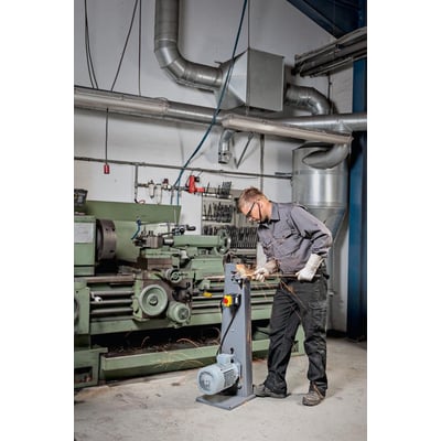 Fein GRIT GKS 75 kompakt-båndsliber i brug i et værksted med en mand, der arbejder på metal og gnister flyver.