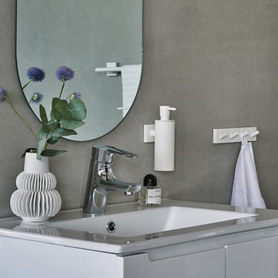 Smedbo House sæbedispenser i mat hvid monteret på en grå betonvæg over en hvid håndvask.