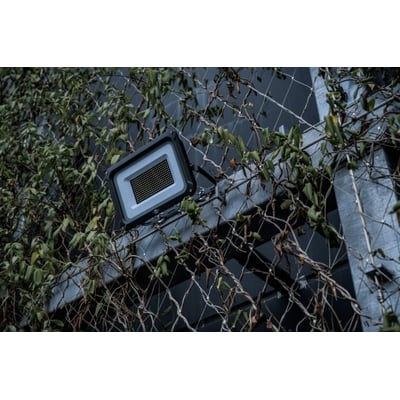 Brennenstuhl 150W LED projektør monteret på en facade med grønne planter og trådnet.