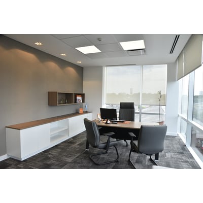 Moderne kontorindretning med skrivebord, stole og hvidt opbevaringsmøbel med trædetaljer foran grå væg.