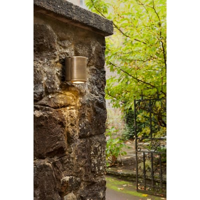 Astro Coastal 7806 Jura Single væglampe monteret på en grov murstensvæg ved indgangen til en have.