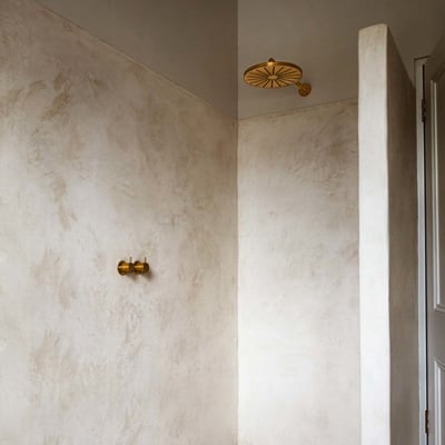 Vola indbygningstermostat med løs afgangsmuffe til hovedbruser og gylden brusehoved monteret på rå, lys væg.