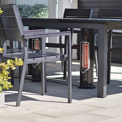 Mensa Heating terrassevarmer IMUS 550W i sort, placeret under et havebord med stole, lyser op med infrarøde varmestråler.