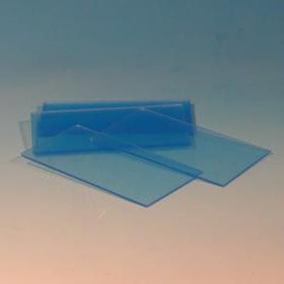 Et bundt klart svejseglas i plexi, 51x108 mm, stablet og liggende på en baggrund med blå gradient.