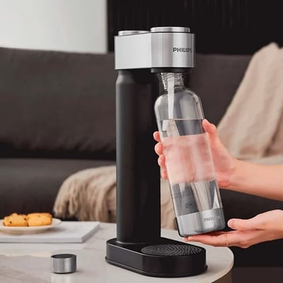 Philips sodavandsmaskine i sort med en glasflaske fyldt med vand, klar til at blive sat i maskinen.