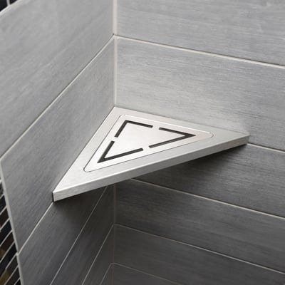 Unidrain Anniversario hjørne sæbehylde i børstet stål monteret i et moderne gråt flisehjørne i en bruseniche.