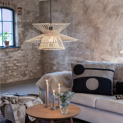 Markslöjd Duplici pendel i naturmateriale, monteret i en hyggelig stue med sofa og stearinlys.