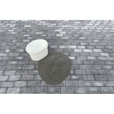 En hvid spand og en bunke A-JOINT Polysand PRO specialfugesand i stone grey placeret på en grå stenbelægning.