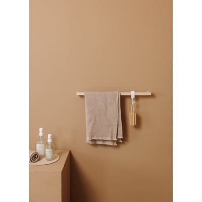Metallbude Vana håndklædestangen i beige, monteret på en sandfarvet væg med et beige håndklæde hængende.