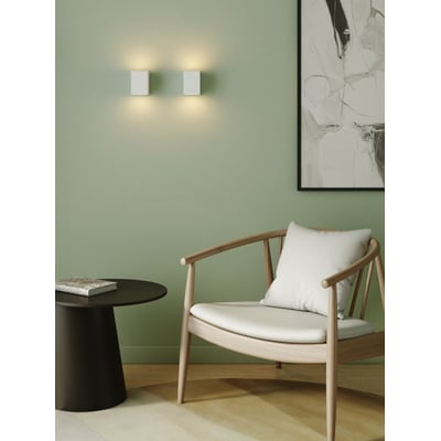 To Astro Lighting Mosto væglamper monteret på lysegrøn væg over et sofabord og en stol.