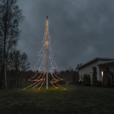 Konstsmide flagstangskæde med 680 varmhvide LED'er på 19 meter, opsat som et juletræ i en have ved et hus.
