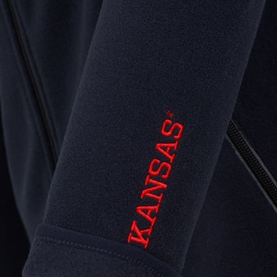 Detaljeret billede af Kansas Evolve Fleece Jakke i marineblå, viser rødt broderet Kansas logo på venstre ærme.