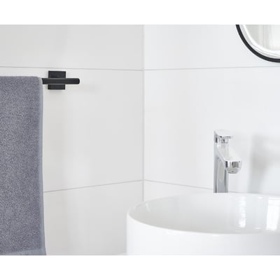 Smedbo House håndklædestang i mat sort messing, monteret på en hvid flisevæg ved siden af en hvid vask og krom vandhane.