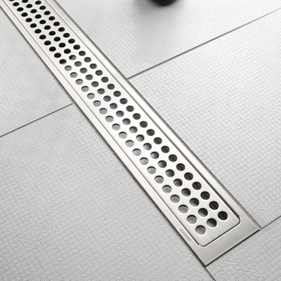 Unidrain fritliggende afløbsarmatur på 1200mm i bejdset stål, monteret i et badeværelsesgulv med grålige fliser.