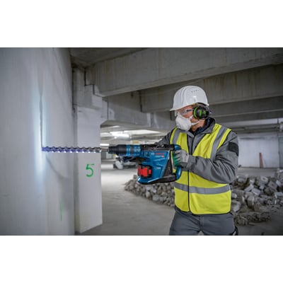 Bosch borehammer GBH 18V-40 C med SDS-max og BITURBO Brushless-teknologi, der borer i betonvæg af en person i sikkerhedsudstyr.