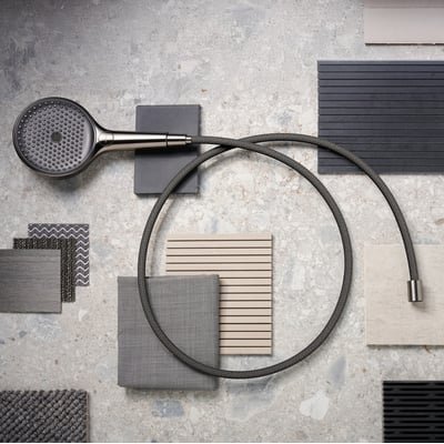 Hansgrohe håndbruserslange i sort krom ligger snoet på en grå marmorbordplade sammen med fliser og stofprøver.