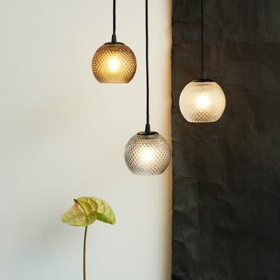 Tre Halo Design Nobb pendler i røgfarvet glas med 125 mm diameter, hænger ved siden af hinanden med lys tændt.