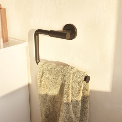 Cosmic håndklædeholder i mat sort finish, vist med et håndklæde hængende på et lyst, tekstureret badeværelsesvæg.