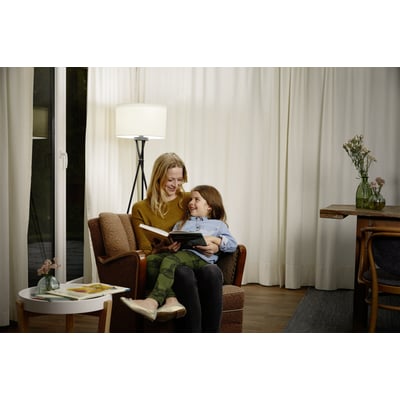 Mor og datter hygger sig med en bog i en stue, oplyst af et blødt lys fra en lampe.