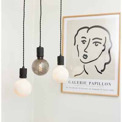 Tre Halo Design COLORS Geo lyskilder hænger ned fra sorte ledninger, med en kunstplakat i baggrunden.