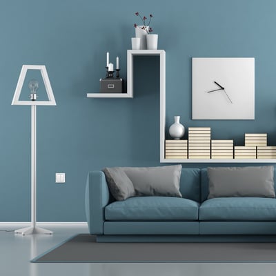 Lauritz Knudsen Friends Of Hue trådløst tryk i hvid, monteret på en blå væg ved siden af en lampe og sofa.