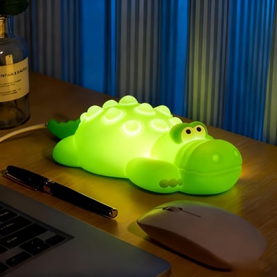 Mochi krokodille-natlampe lyser klart grønt på et skrivebord med computer og mus.