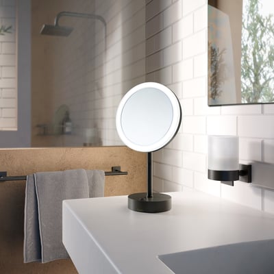 Smedbo Outline barber-/sminkespejl med LED-lys, 20 cm i diameter, mat sort finish på bordplade ved vask.
