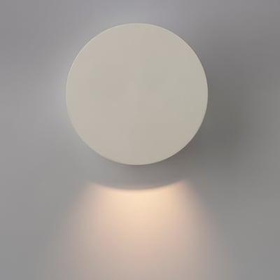 ANTIDARK Dot W120 væglampe i hvid, med lys der skaber en blød glød på den grå væg.