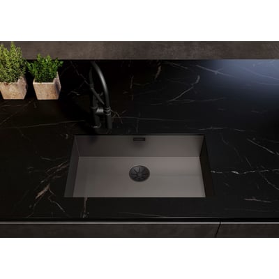 Blanco Infino afløb i sort mat rustfrit stål indbygget i en mørk køkkenbordplade med hane og grønne planter i baggrunden.
