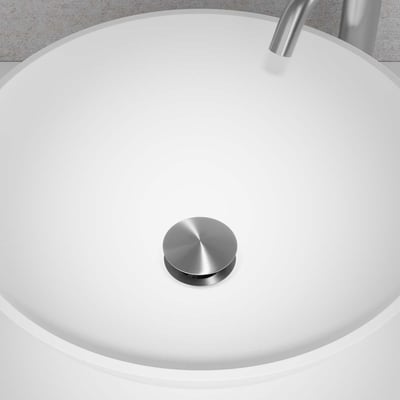 Primy Steel Duo Pop-up bundventil i børstet stål monteret i en hvid håndvask, med synlig vandhane i baggrunden.
