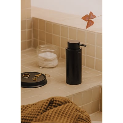 Cosmic Logic sæbedispenser i mat sort med 200 ml kapacitet, placeret på et badeværelsesbord med bomuldspads og smykker.