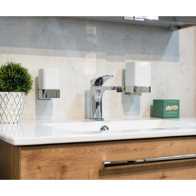 Smedbo ice sæbedispenser i poleret krom og hvidt porcelæn placeret ved siden af en vandhane på en vask.