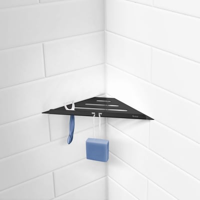 Smedbo Sideline sort hjørnehylde i rustfrit stål, vist monteret i et badeværelse med hvide fliser og badehåndklæde samt svamp hængende.
