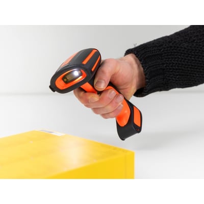 DeLock 1D/2D barcode scanner i hånden, der scanner en gul pakke, med orange og sorte detaljer og en aktiv lysdiode.