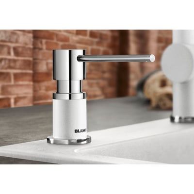 BLANCO LATO sæbedispenser i klippegrå SILGRANIT® og skinnende krom, monteret ved siden af en hvid køkkenvask med murstensvæg i baggrunden.