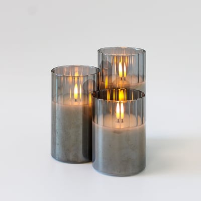 Tre LEDlife LED bloklys i røgfarvet glas med lysende flammeeffekt på en hvid baggrund.