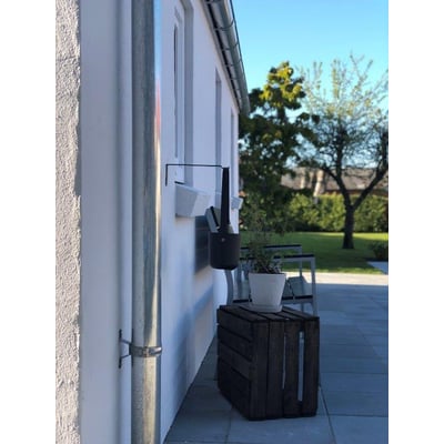 Plastmo 12" endebund i zink monteret på husmur med nedløbsrør og grønne planter i forgrunden.